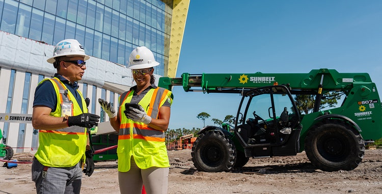 Un hombre y una mujer en una obra de construcción, una máquina de Sunbelt en el fondo