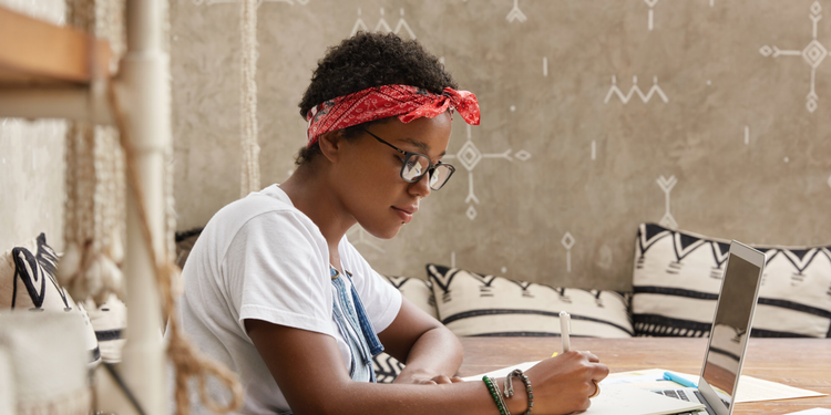 A woman in a living room looks at her laptop and writes notes about A/B testing.