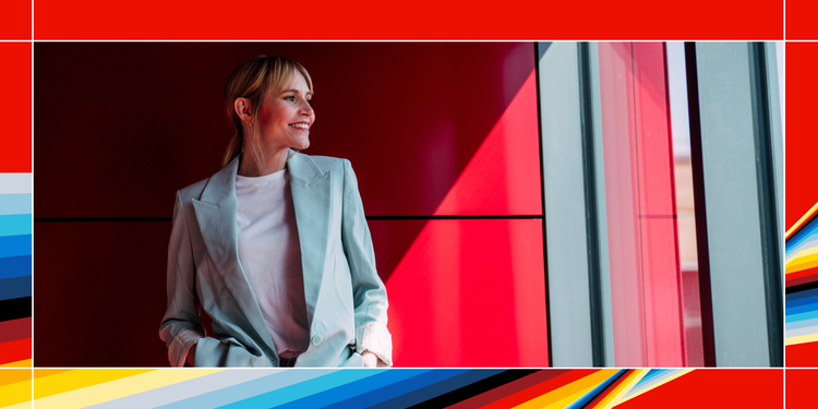 Woman smiling while standing against a red building with colourful graphic border around the image.