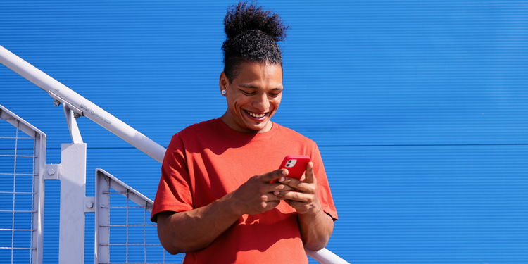 Person using a smartphone in front of a bright blue wall.