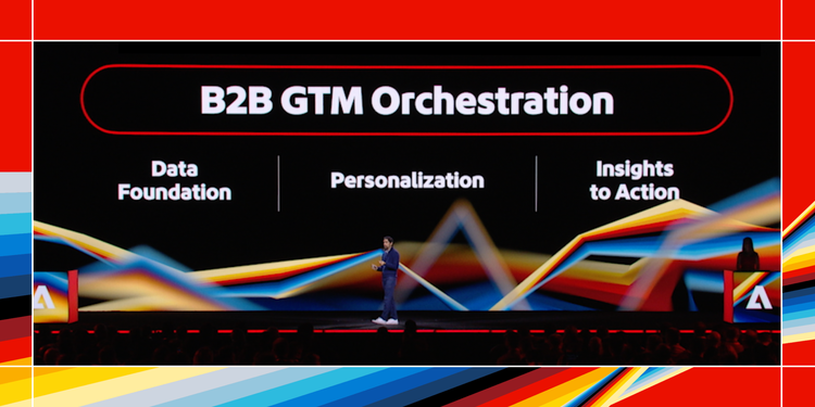 Presenter on stage at Adobe Summit 2025. Presentation visuals outline B2B GTM orchestration.