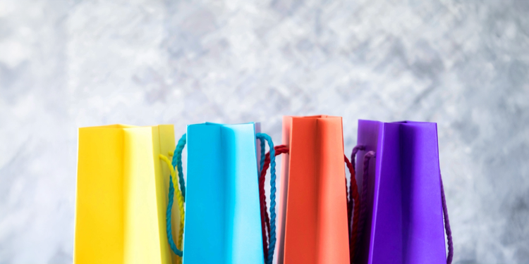Row of colourful shopping bags in yellow, blue, red and purple against a soft grey background.
