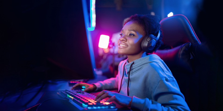 A gamer wearing headphones and a blue hoodie plays an online game on a computer.