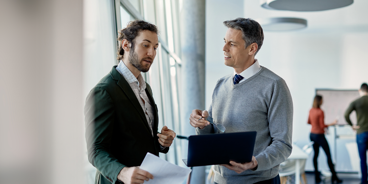 Two business executives in an office discuss industry benchmarks.