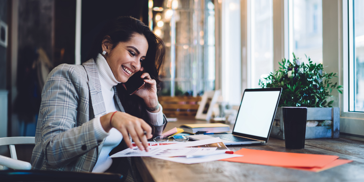 A female business professional talking on the phone analyzes her website's ecommerce bounce rate using a laptop and paper diagrams.