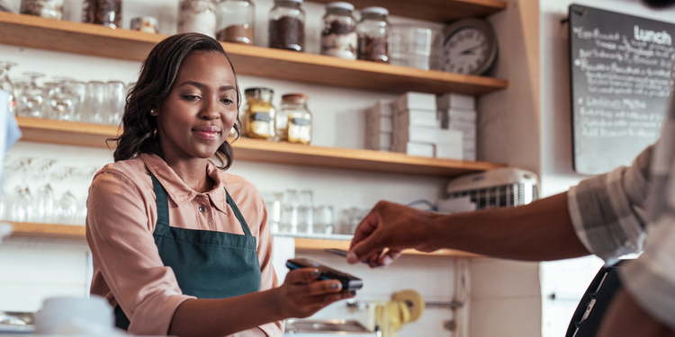 A cashier in a cafe holding a device for payment processing while a customer taps a card.