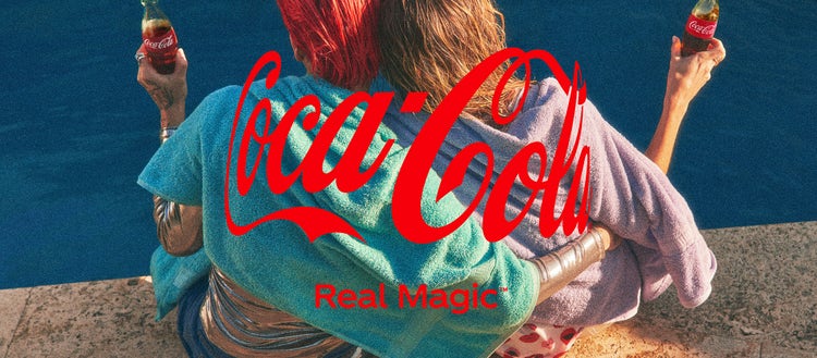 Two friends wrapped in towels sit close together beside a pool, each holding a glass bottle of Coca-Cola. The image captures a casual, warm moment, overlaid with Coca-Cola’s logo and the tagline 'Real Magic.'