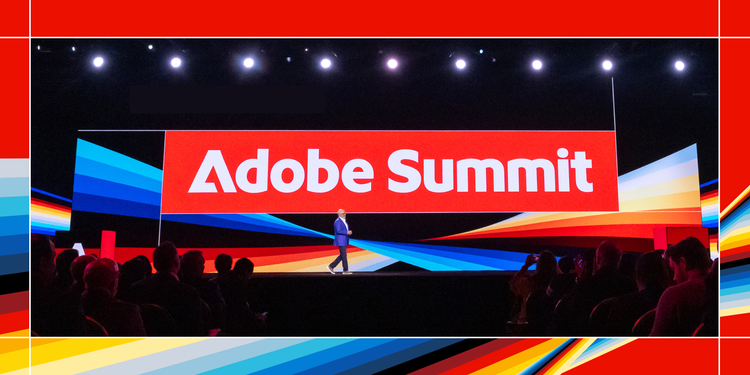 A speaker stands on stage in front of a large screen displaying 'Adobe Summit' in bold white letters on a red background. The stage is lit dramatically, with colorful abstract streaks of red, blue, yellow, and black extending across the screen and stage floor. An audience is seated in the foreground, watching the presentation.