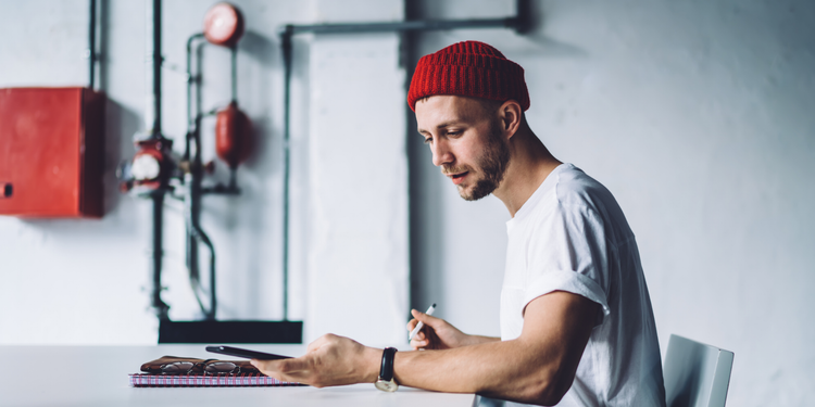 A man wearing a white shirt and red beanie looking at a mobile phone to prepare for Cyber Monday consumer trends.