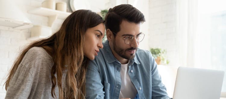 Focused young couple calculating bills, discussing planning budget together, serious wife and husband looking at laptop screen, using online banking services and calculator, checking finances