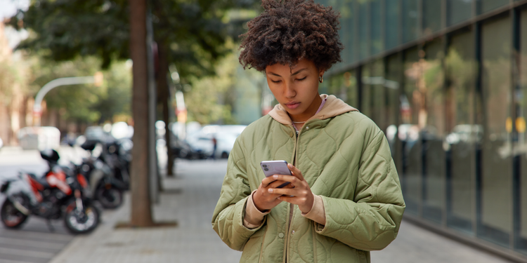 A young person wearing a green coat views content marketing on a mobile phone.