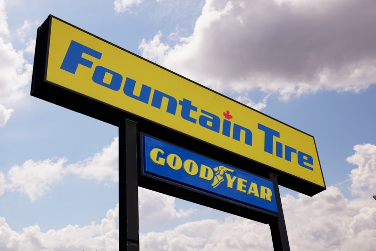 Photo of a Fountain Tire storefront sign with the Goodyear logo against a partly cloudy sky.