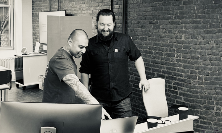 Ephraim Gerard Cruz and Christopher Grove from Xfinity Creative look at computer monitors in an office.