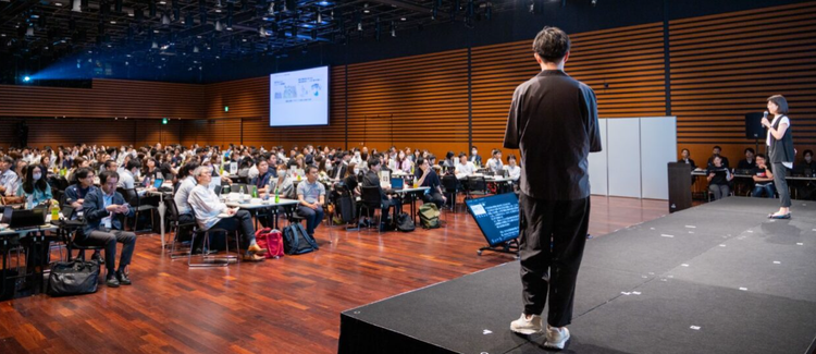 A person standing on a stage in front of a large group of people Description automatically generated