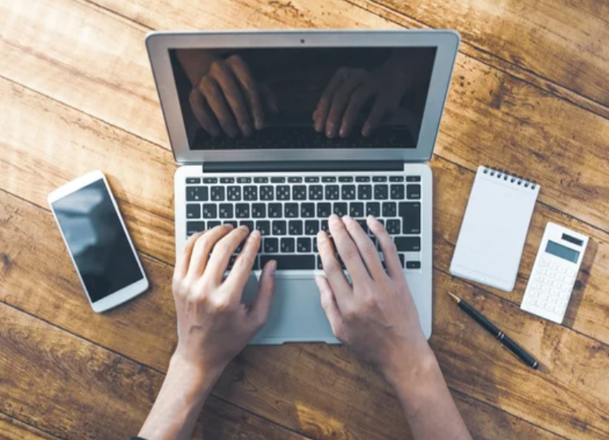 Typing on a laptop, mobile phone to the left on a desk