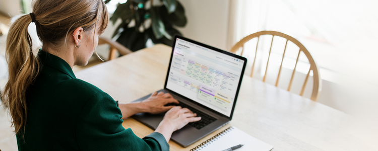 A female business professional sitting at a table uses a laptop to manage projects with Adobe Workfront.