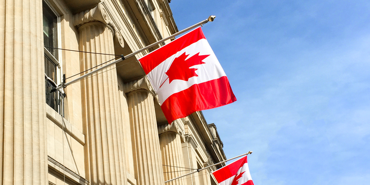 Canadian flags wave in front of a neoclassical government building.
