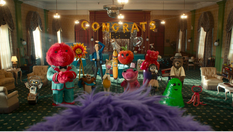 Animated image of a group of fun fictional characters — including a pink furry monster in a light blue suit, a skinny character in plaid suit with a sunflower head, a banana with a head band and others.