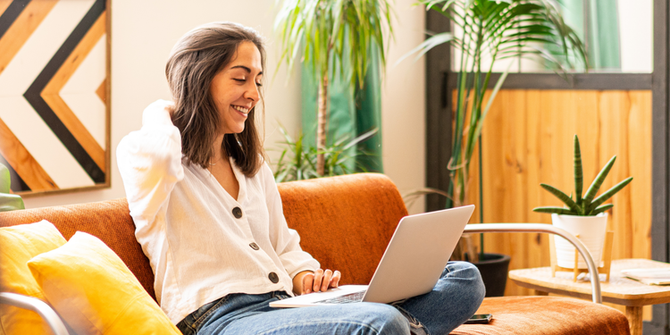 A person is smiling and sitting on a sofa with their work laptop.